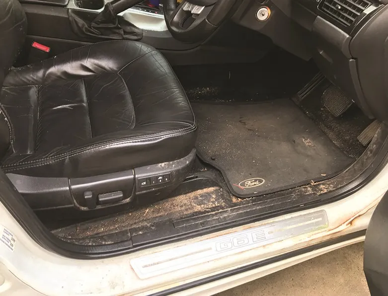 Car footwell with heavily soiled carpet, dirt through the seat rails and door sill