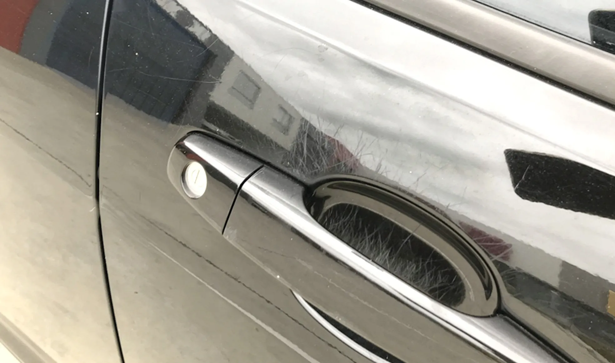Dark car door with a spray of fine key and fingernail scratches around the handle